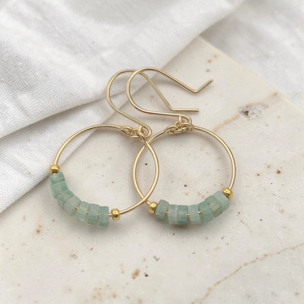 Gold hoop earrings with green aventurine beads on a marble surface
