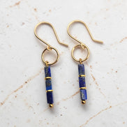 A pair of gold dangle earrings with rectangular lapis lazuli beads, displayed on a light textured marble background.