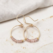 Gold hoop earrings with pink beaded accents on a marble surface.