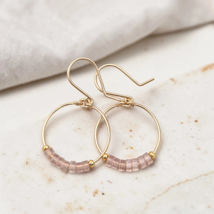 Gold hoop earrings with pink beaded accents on a marble surface.