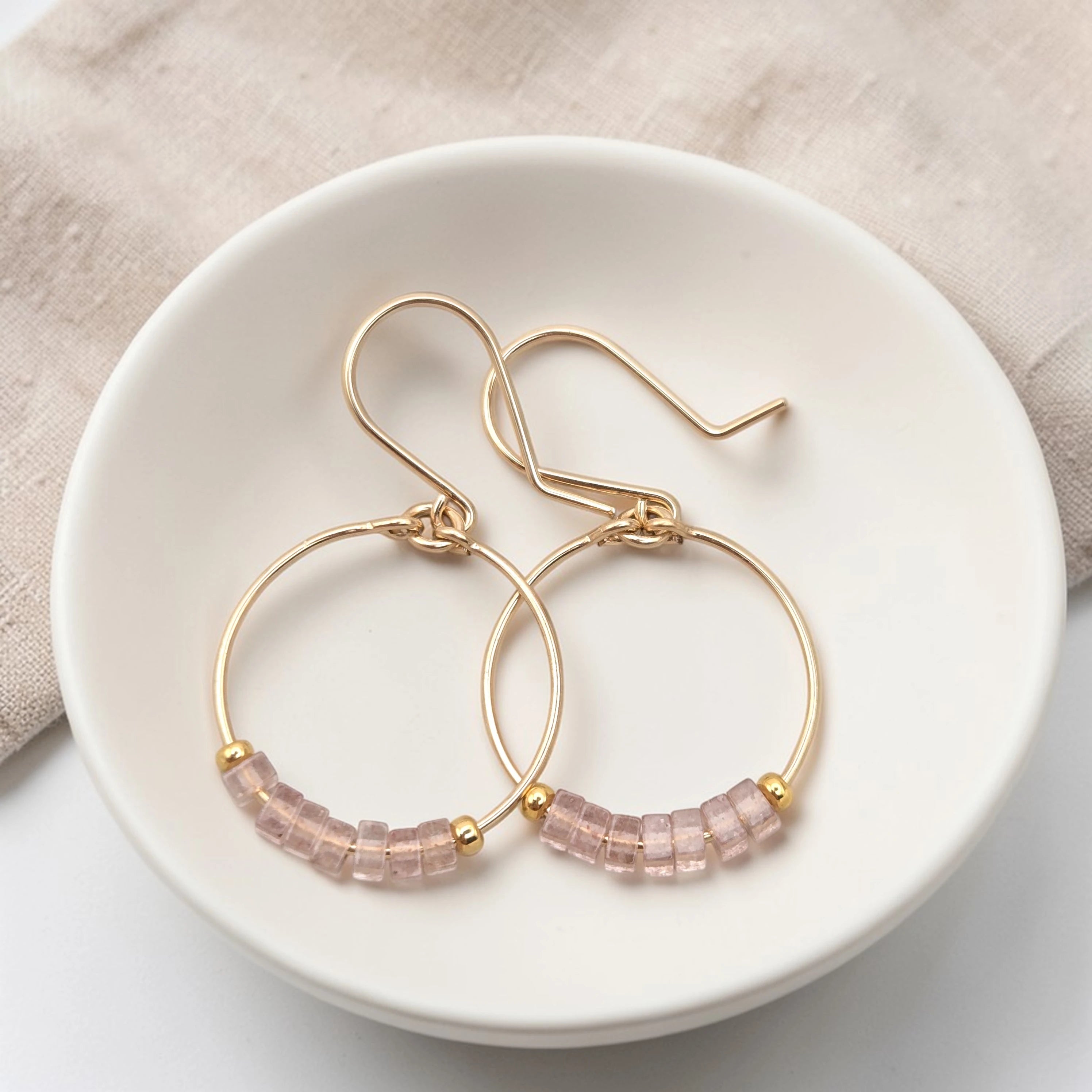 Gold hoop earrings with pink beaded accents on a white dish.