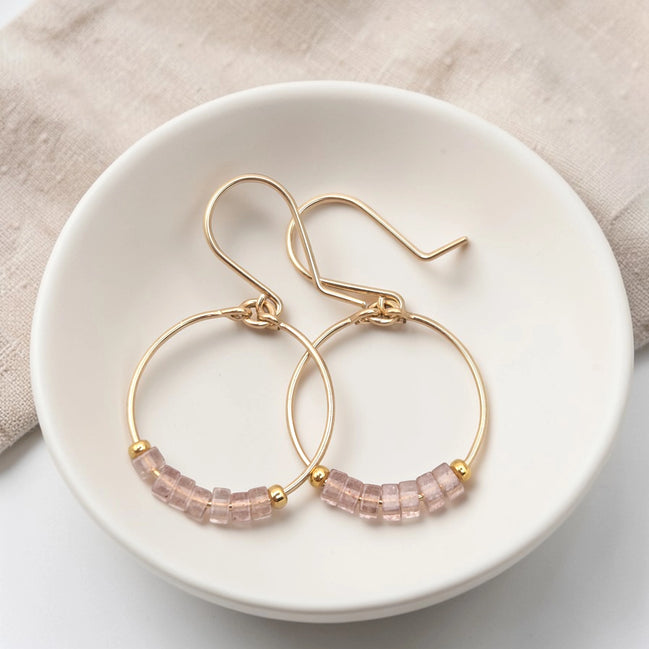 Gold hoop earrings with pink beaded accents on a white dish.