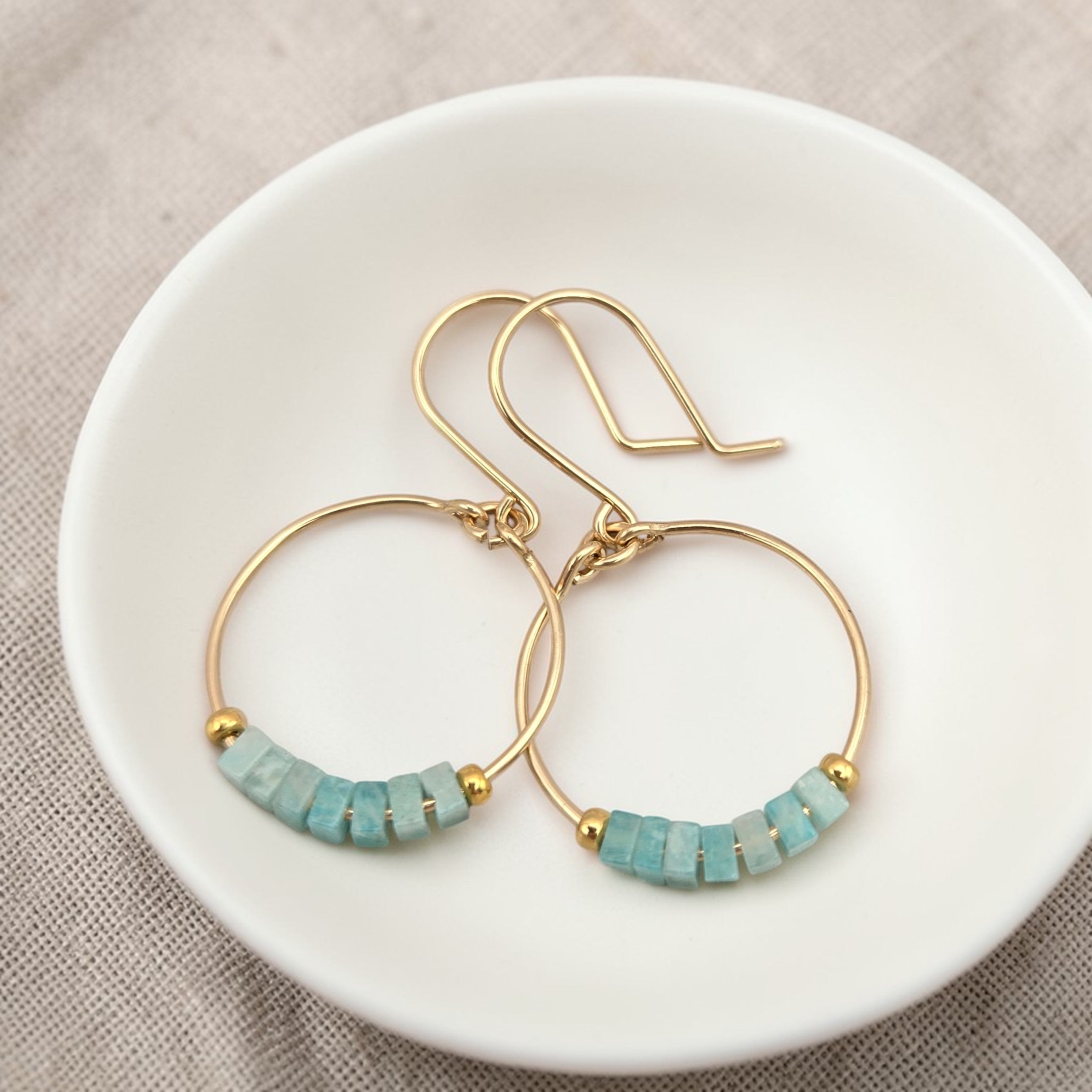 Gold hoop earrings with amazonite beads on a white dish.