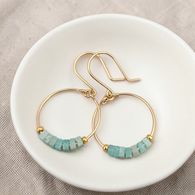 Gold hoop earrings with amazonite beads on a white dish.