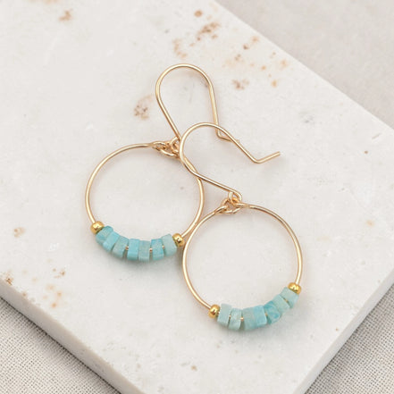 Gold hoop earrings with amazonite beads on a marble surface