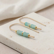 Gold earrings with amazonite beads on a beige stone surface
