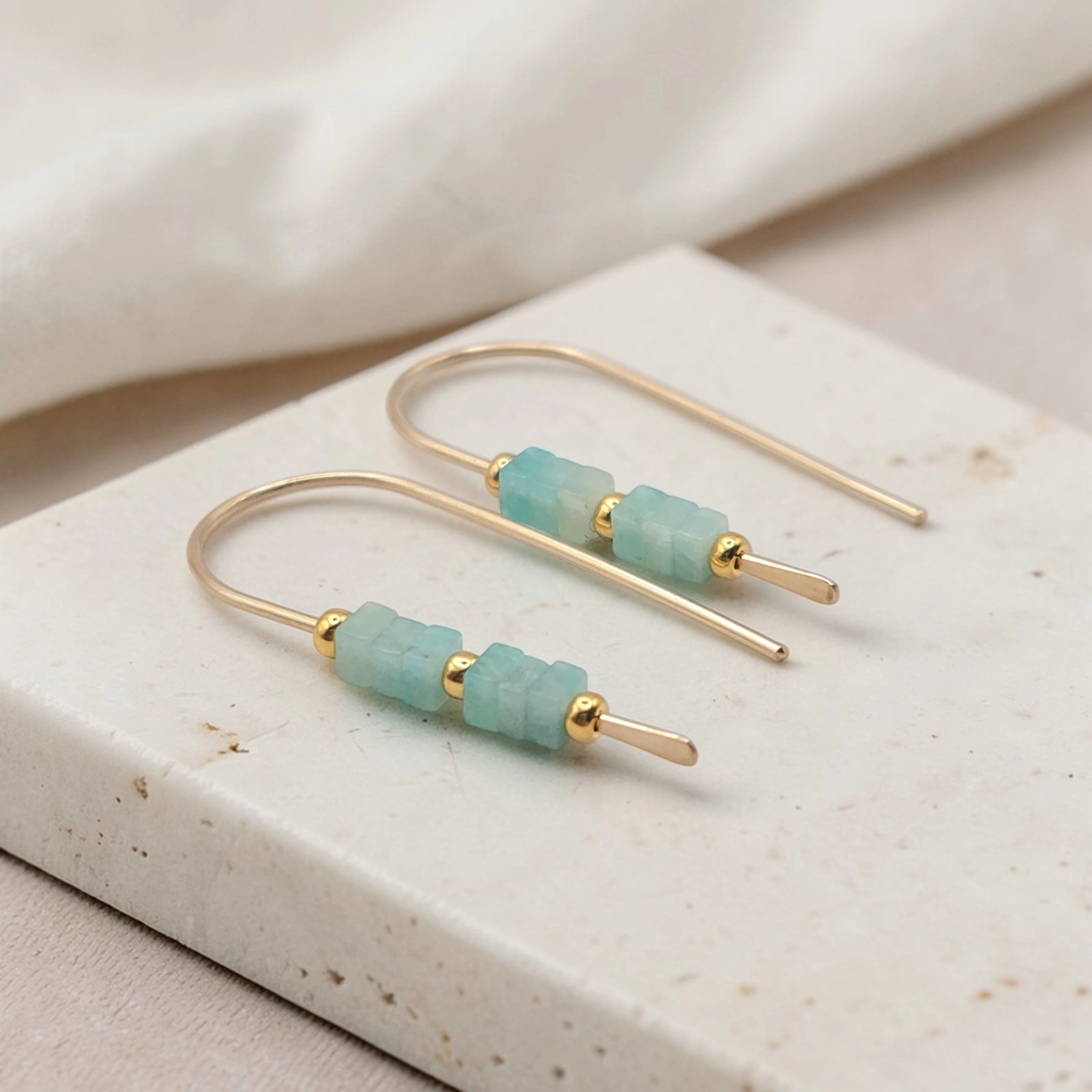 Gold earrings with amazonite beads on a beige stone surface