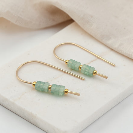 Gold earrings with green beads on a beige fabric background