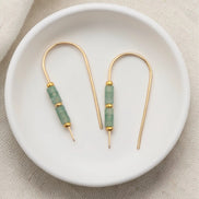 Gold and green beaded earrings on a white dish with a beige fabric background