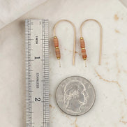 Pair of gold earrings with brown beads next to a ruler and quarter for scale on a marble surface.