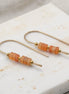 Pair of gold earrings with orange beads on a marble surface