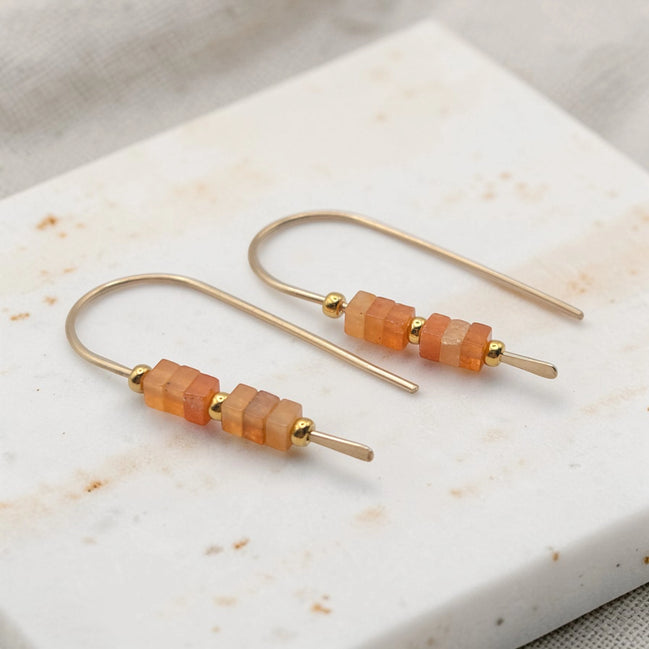 Pair of gold earrings with orange beads on a marble surface