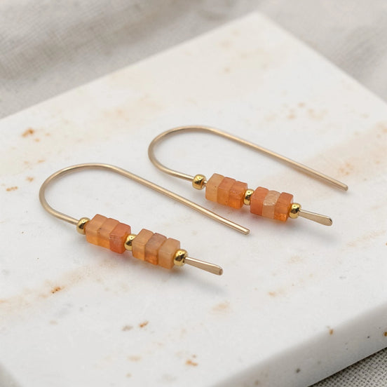 Pair of gold earrings with orange beads on a marble surface