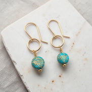 Gold earrings with turquoise beads on a marble surface