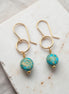 Gold earrings with turquoise beads on a marble surface