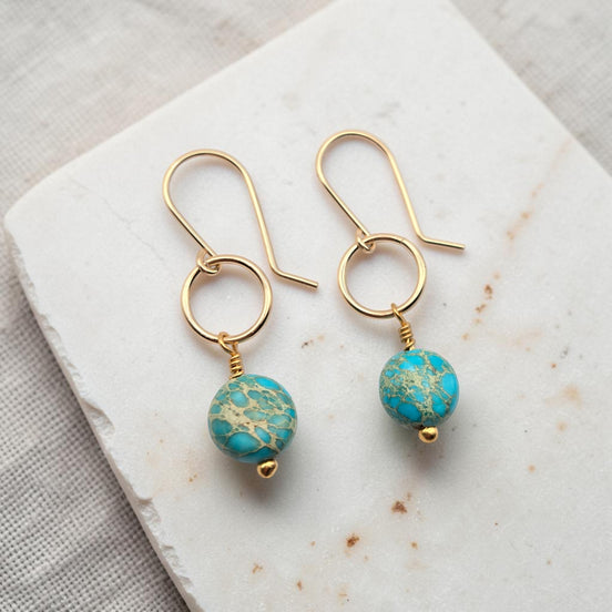 Gold earrings with turquoise beads on a marble surface