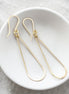 Gold earrings on a white dish with a textured gray background