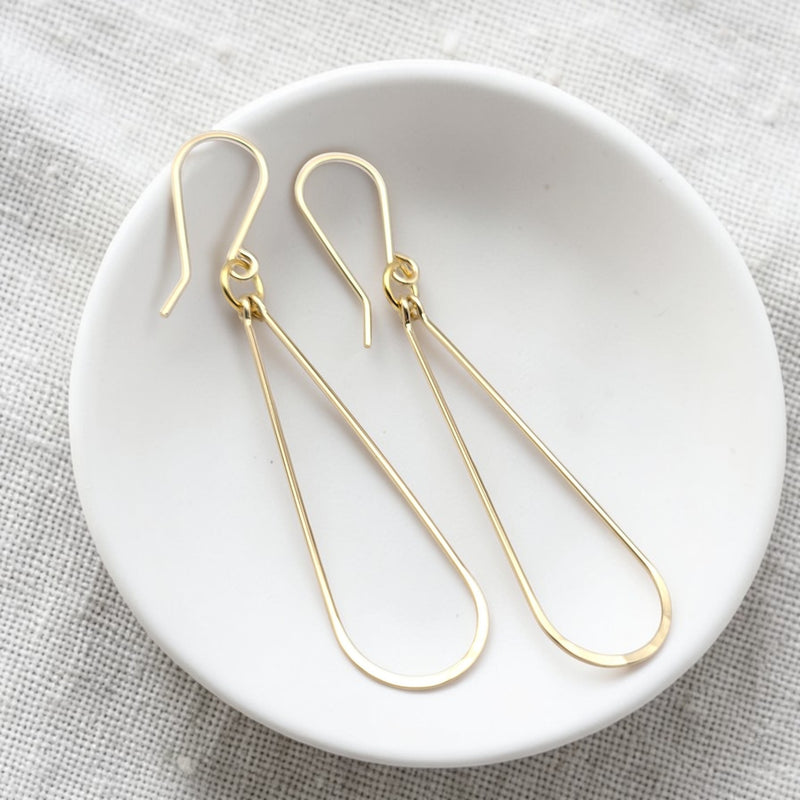 Gold earrings on a white dish with a textured gray background