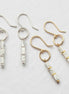 Four dangle earrings arranged on a light textured background. Two earrings have silver-tone hooks and bezel-set white marbled beads, while two have gold-tone hooks and bezel-set white marbled beads with small gold accents.