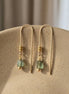Gold earrings with green beads on a beige surface