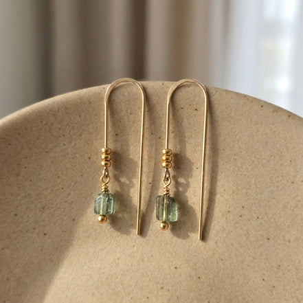 Gold earrings with green beads on a beige surface