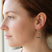 Close-up of a woman wearing a gold hoop earring with blue stones.