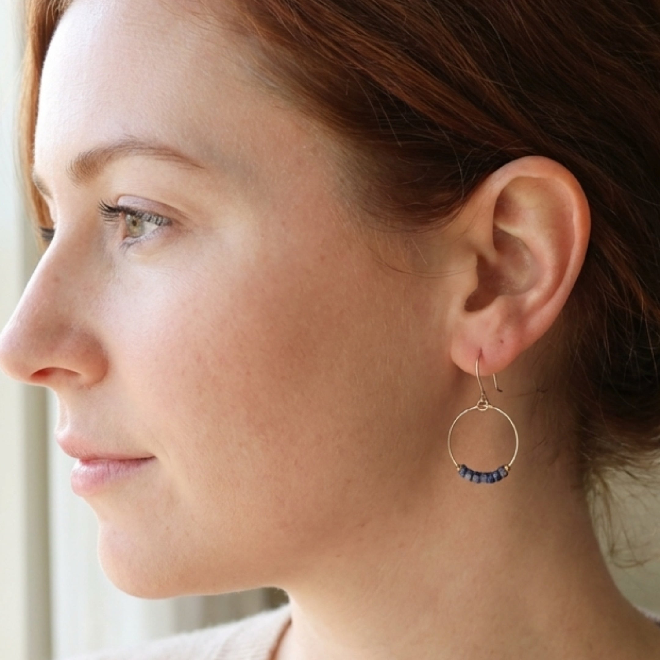 Close-up of a woman wearing a gold hoop earring with blue stones.