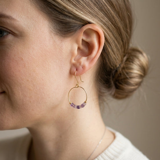 Close-up of a woman wearing gold hoop earrings with purple beads.