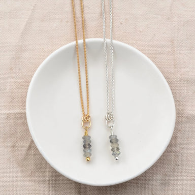 Two necklaces with gemstone pendants on a white dish against a beige background