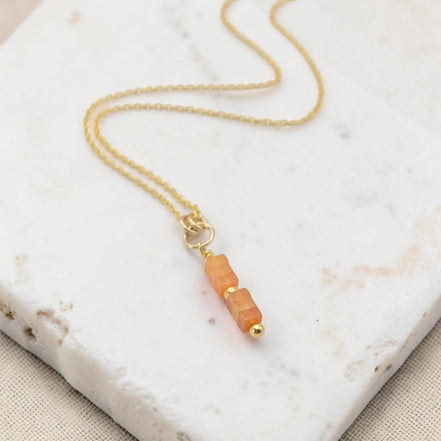 Gold necklace with a peach-colored pendant on a marble surface