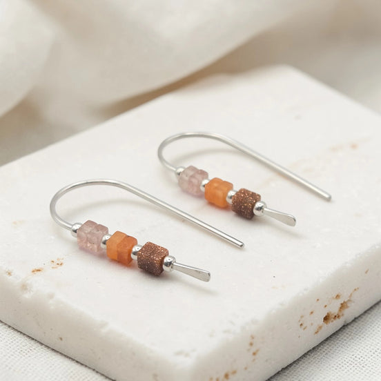 Silver earrings with colorful beads on a white stone surface