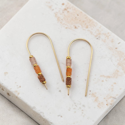Gold earrings with brown beads on a marble surface
