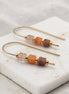 Pair of gold earrings with colorful beads on a marble surface