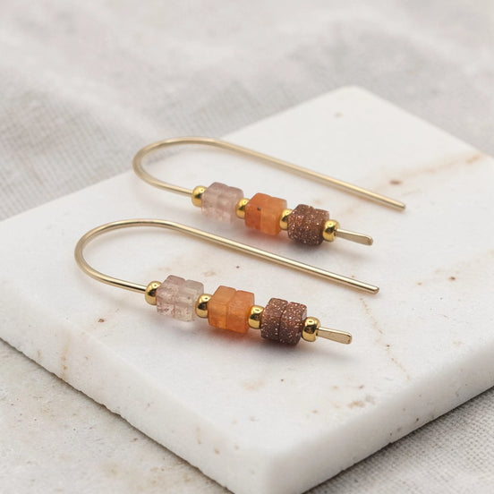 Pair of gold earrings with colorful beads on a marble surface
