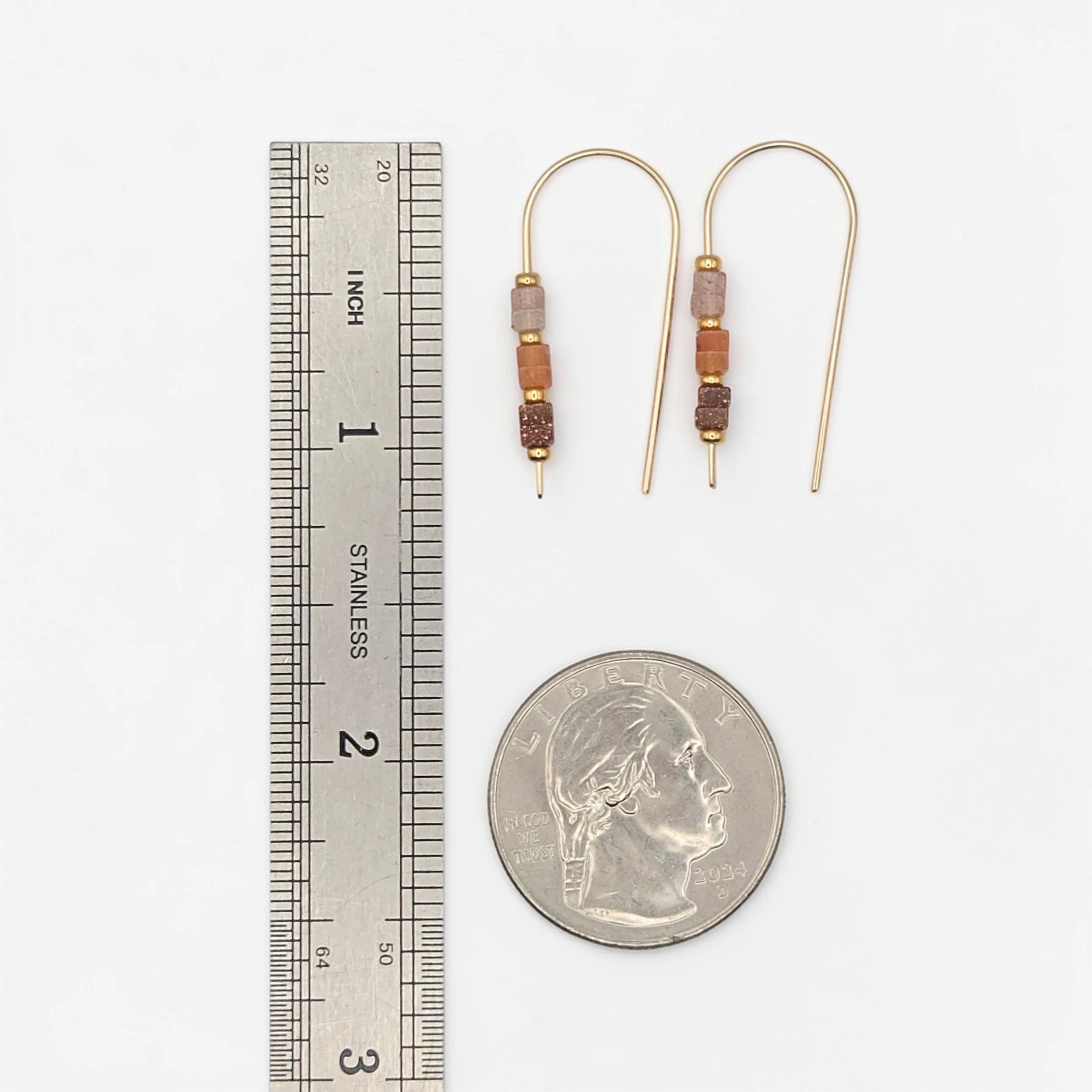 Pair of beaded earrings next to a ruler and a quarter for scale on a white background