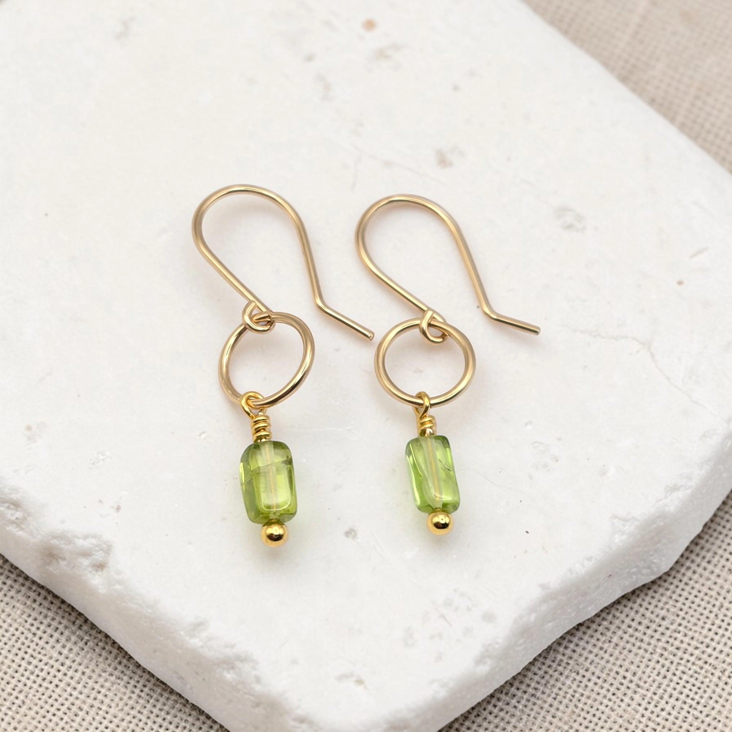 Gold earrings with green peridot beads on a textured white surface