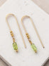 Gold earrings with peridot beads on a white stone surface