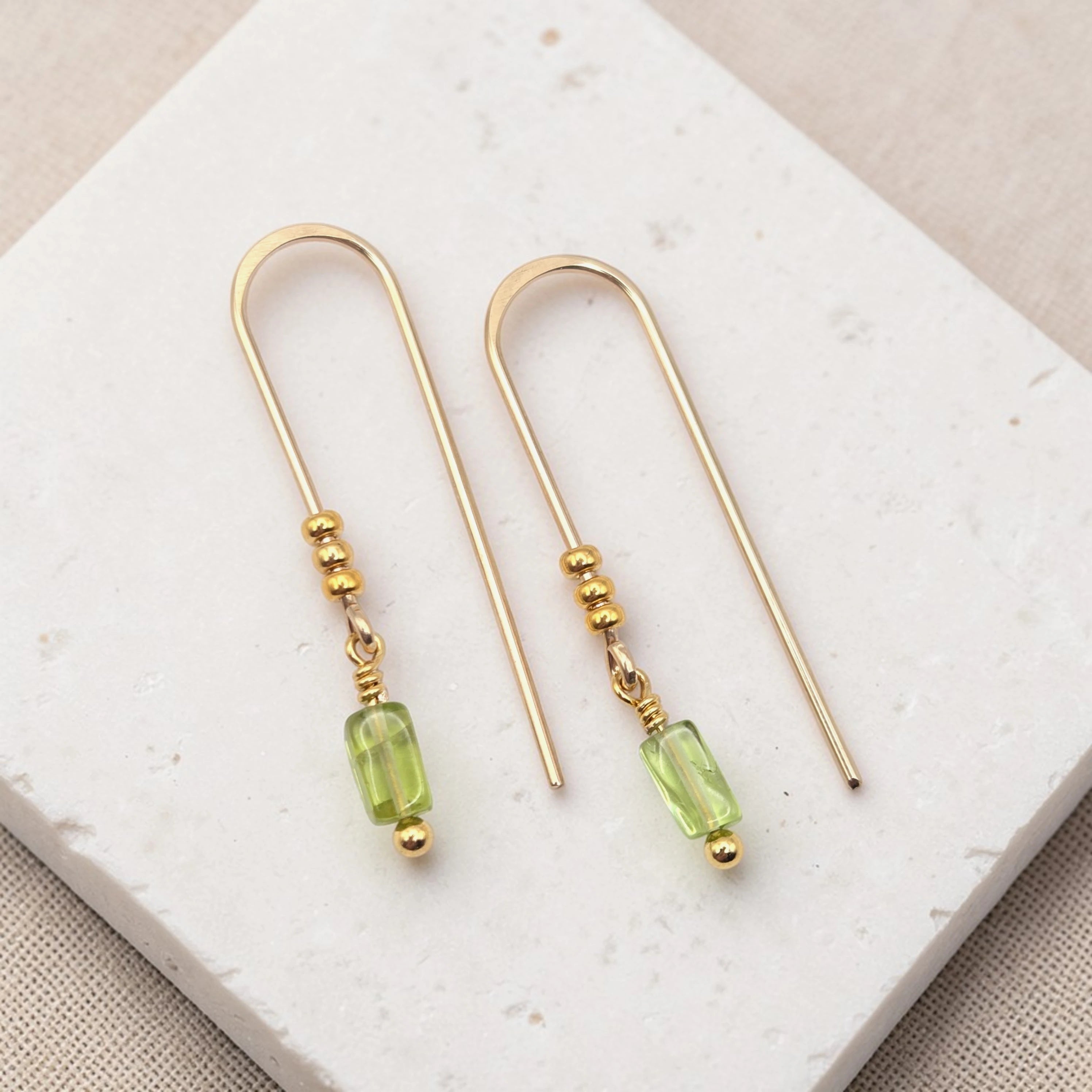 Gold earrings with peridot beads on a white stone surface