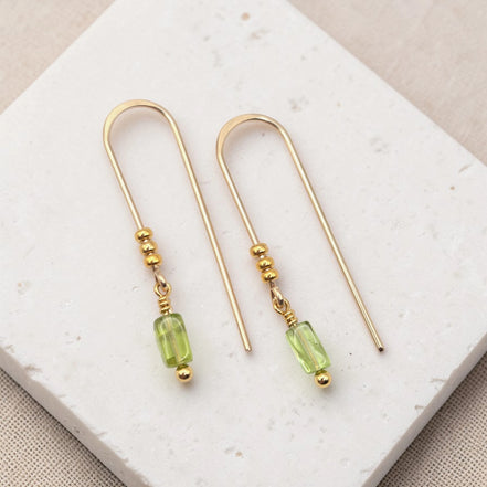 Gold earrings with peridot beads on a white stone surface