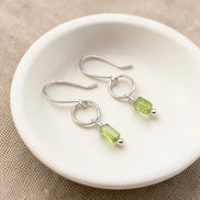 Silver earrings with green  peridot beads on a white dish