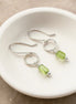 Silver earrings with green  peridot beads on a white dish