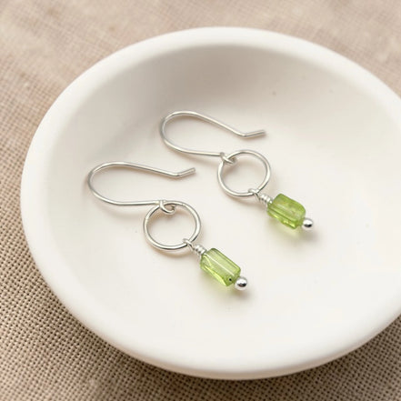 Silver earrings with green  peridot beads on a white dish
