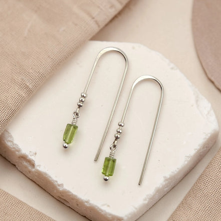 Silver earrings with peridot beads on a white stone surface