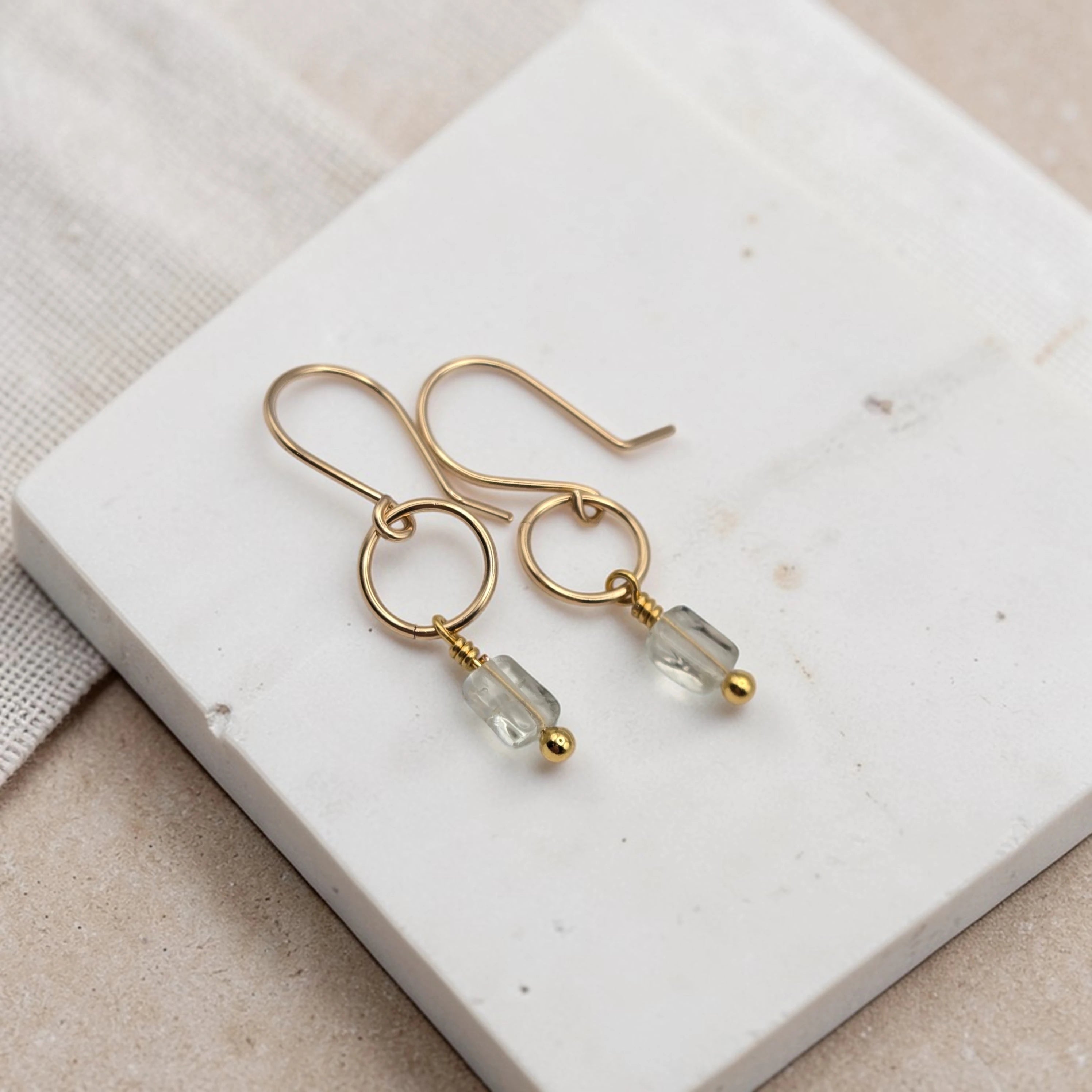 Gold earrings with clear beads on a white stone surface