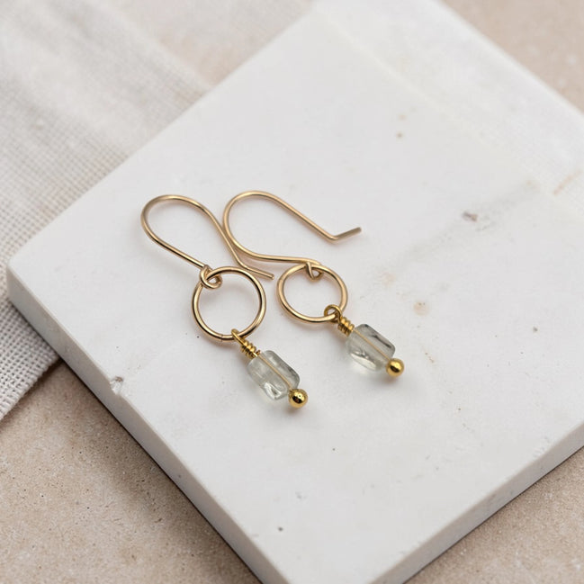 Gold earrings with clear beads on a white stone surface