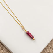 Gold necklace with a red gemstone pendant on a white surface
