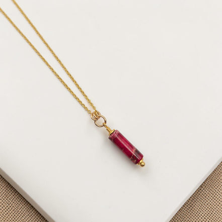 Gold necklace with a red gemstone pendant on a white surface