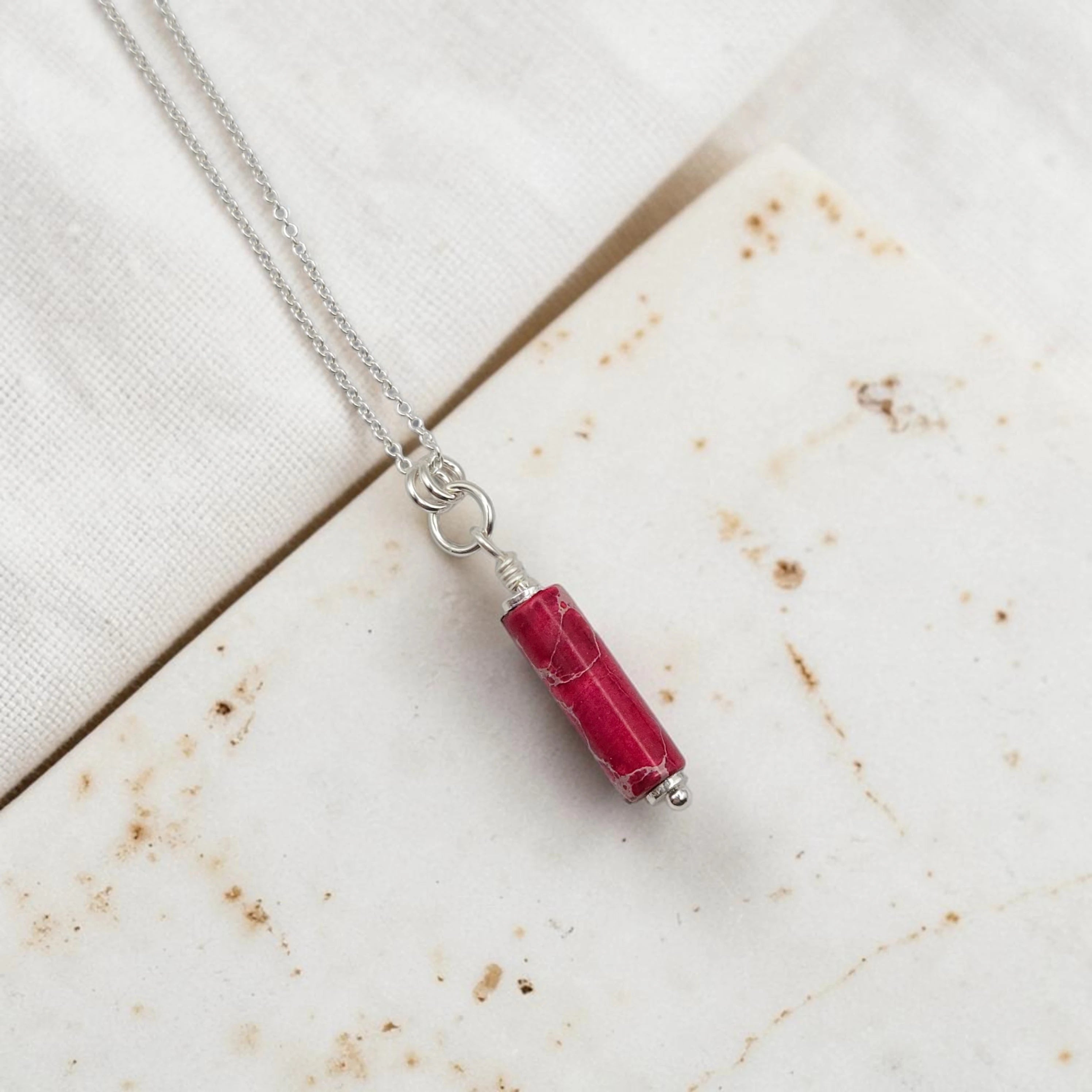 Necklace with a red cylindrical pendant on a textured surface