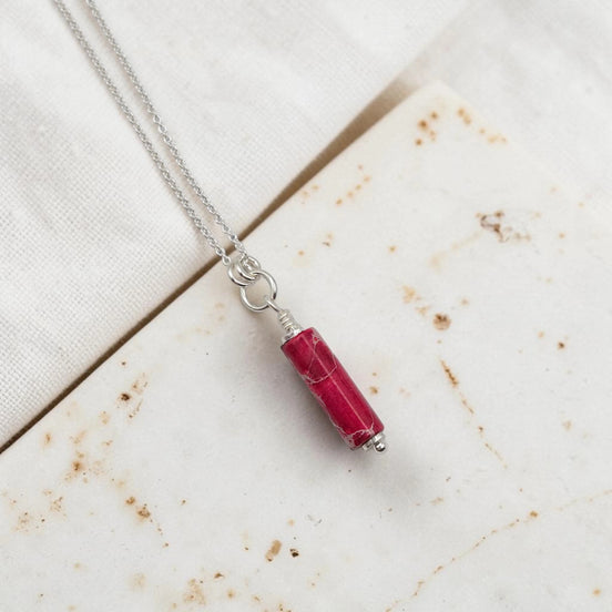 Necklace with a red cylindrical pendant on a textured surface