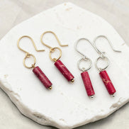 Two pairs of earrings with red cylindrical stones on a white stone surface
